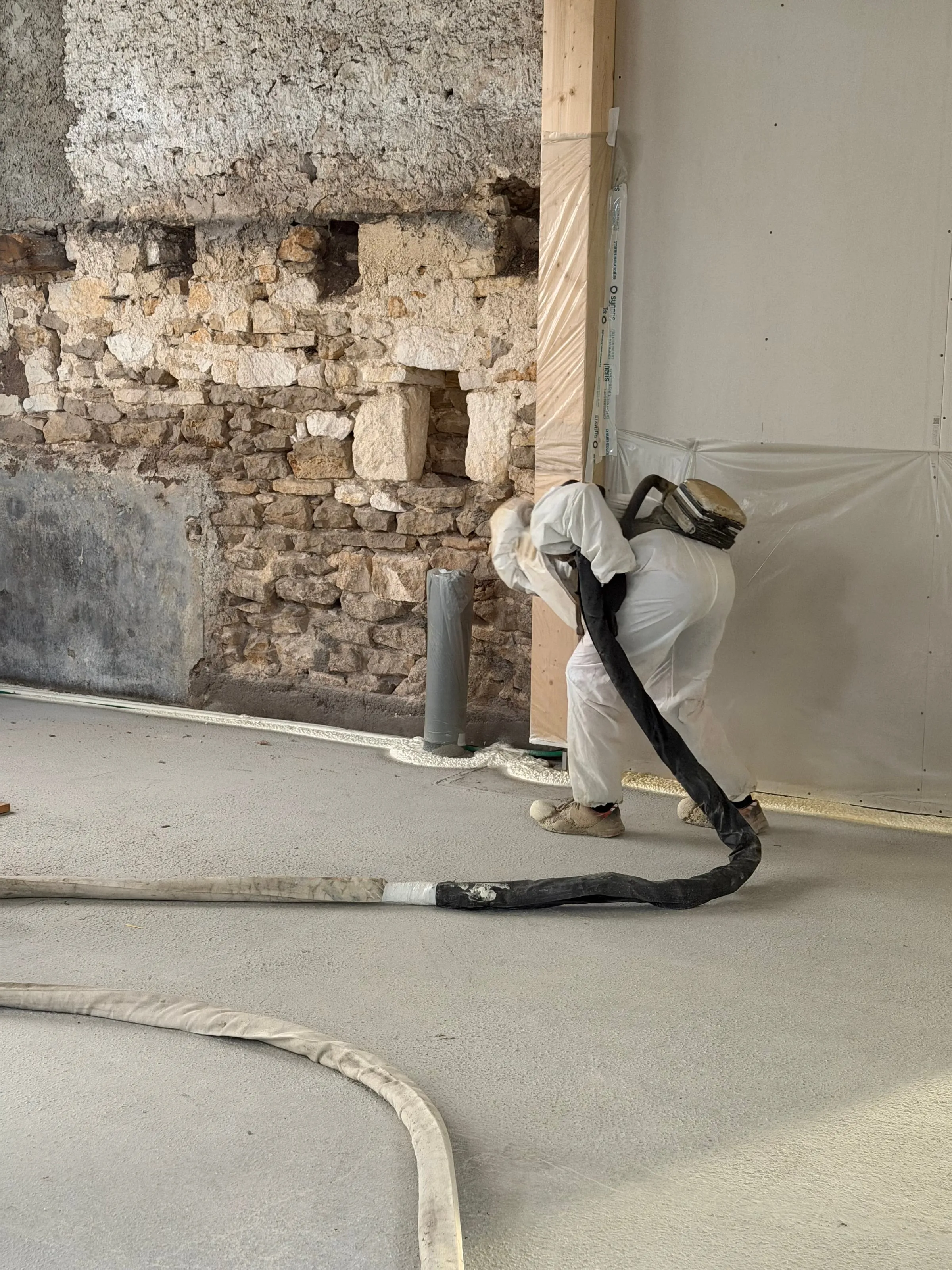 Applicateur Isolatech en pleine projection polyuréthane sur mur en pierre apparente, chantier en production · Pérouse · Isolatech